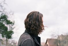 a man with long hair standing in front of a house and looking up at the sky