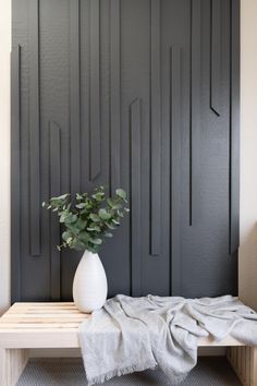 a white vase sitting on top of a wooden bench next to a wall with black panels