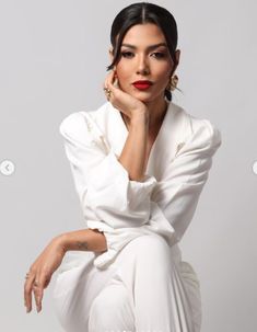 a woman sitting on top of a white chair with her hand under her chin and looking at the camera