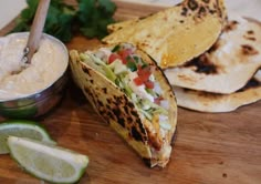 some tacos are sitting on a cutting board next to a small bowl of dip