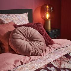 a bed with pink sheets and pillows next to a lamp on a nightstand in a bedroom