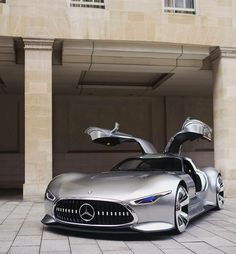 a silver mercedes sports car parked in front of a building with its doors open and it's hood up