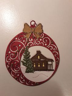 a christmas ornament hanging on the wall with a house and tree in it