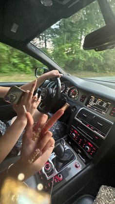 two people driving in a car with their hands on the steering wheel and one person holding up a peace sign