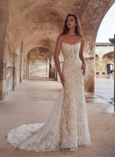 a woman standing in an archway wearing a wedding dress with flowers on the skirt and straps