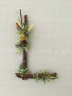 the letter l is made up of branches, flowers and pineconis with leaves