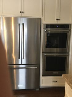 a stainless steel refrigerator and oven in a kitchen with white cabinets, wood flooring and marble counter tops