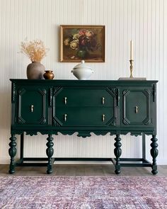 a green cabinet sitting on top of a rug in front of a painting and vase