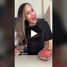 a woman holding an apple and smiling at the camera while wearing a t - shirt