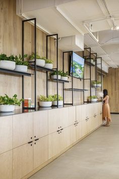 a woman standing in front of a wall filled with potted plants and hanging planters