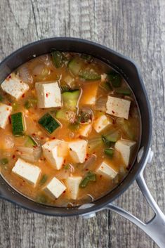 a pan filled with tofu and vegetables sitting on top of a wooden table next to a spoon