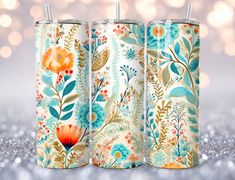 three floral tumbles with straw tops on a glittery surface, one is blue and the other is orange