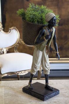 a figurine holding a potted plant on top of a table