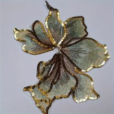 an embroidered flower with gold and silver sequins is shown on a gray background