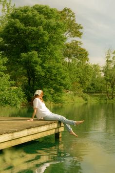 a woman is sitting on a dock by the water