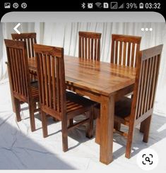 a wooden table with six chairs and one bench in front of white curtained background