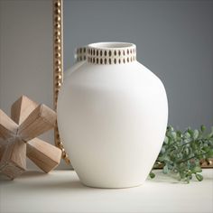 a white vase sitting on top of a table next to a mirror and wooden object