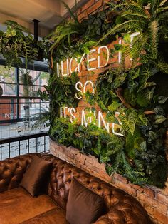 a couch sitting in front of a brick wall covered with plants and neon signs that read, kicked it so it's mine