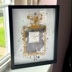 a framed photograph of a chanel perfume bottle in front of a window with grass outside