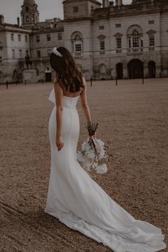 a woman in a white wedding dress holding a bouquet and looking down at the ground