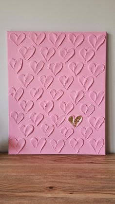 a pink painting with hearts on it sitting on top of a wooden shelf next to a wall