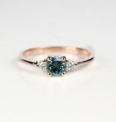 an engagement ring with a blue diamond and three diamonds on the band, set in 18k rose gold