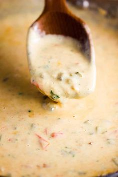 a wooden spoon filled with cheese sauce on top of a pan