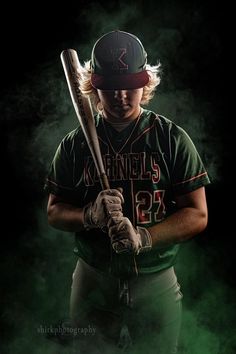 a baseball player is holding a bat in his right hand and wearing a green uniform