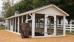 a small white building with windows and a barrel in the dirt near a fenced off area