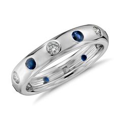 a white gold ring with blue sapphires and diamonds on the side, in front of a