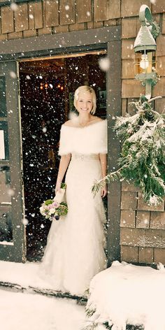 a woman standing in front of a doorway with snow falling on her and holding a bouquet