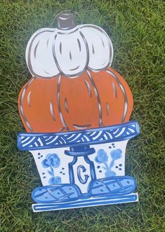 a painted pumpkin sitting on top of a blue and white bowl in the middle of grass