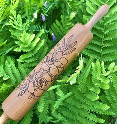 a wooden baseball bat with flowers on it sitting in the grass next to green plants