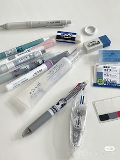 various pens and markers are laid out on a white surface, including one pen with ink