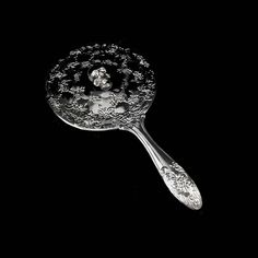 a silver spoon with a lady on it's face in the center, against a black background