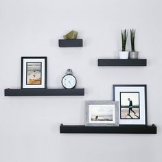 three black floating shelves with pictures and photos on them, one is holding a clock