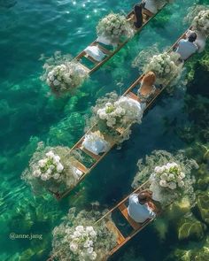 two rows of boats filled with flowers floating on top of the blue water next to each other