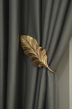 a gold leaf is hanging on the curtain in front of a window with grey drapes