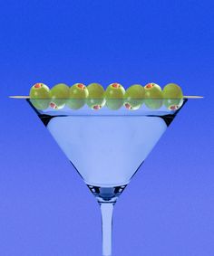 a martini glass filled with green olives on a purple background and blue sky in the background