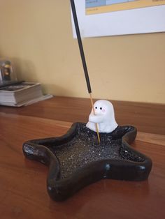 a small white ghost sitting on top of a black star shaped object with a stick in it's mouth