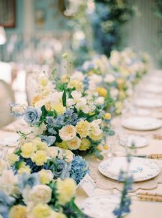 a long table with blue and yellow flowers on it is set for a formal dinner