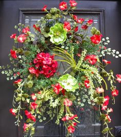 a wreath with red and green flowers hanging from it's side on a door