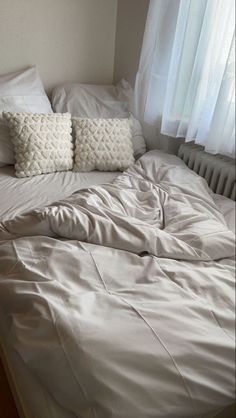 an unmade bed with white sheets and two pillows on top of it in front of a window