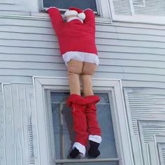 a person dressed as santa claus hanging from the side of a house with his legs in the air