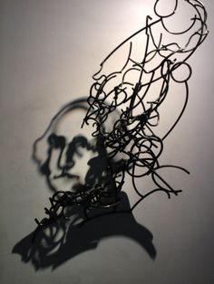 the shadow of a person's head is cast on a white wall with black wire