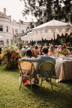 people sitting at tables in the grass under an umbrella