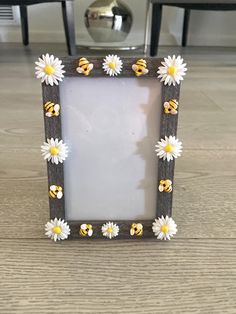 a small wooden frame with daisies and bees on the front, sitting on a table