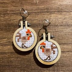 a pair of hoop earrings with an animal cross stitched on the front and back