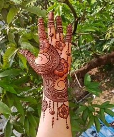 a hand with henna designs on it and some leaves in the back ground behind it