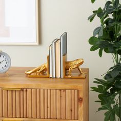 a wooden dresser with books and a clock on it next to a potted plant